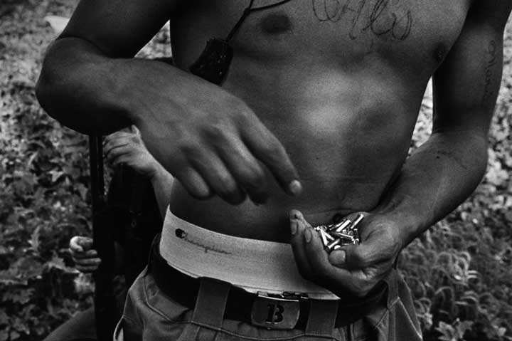 A youth holds bullets to load the gun these gang members are using for target practice.  Copyright © Donna DeCesare, 1996Un jóven sostiene unas balas para cargar una pistola que estos pandilleros usan para practicar tiro al blanco.